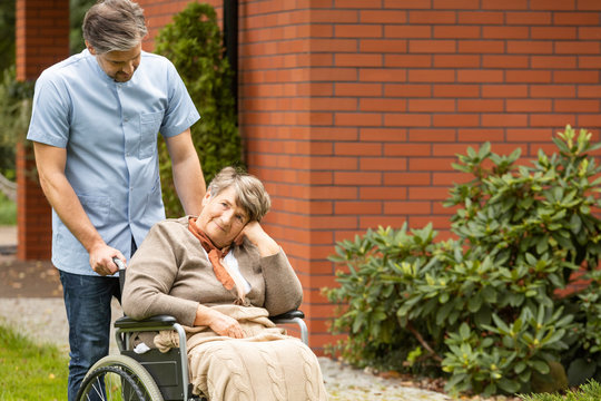 Male Nurse Supporting Disabled Senior Woman In The Wheelchair