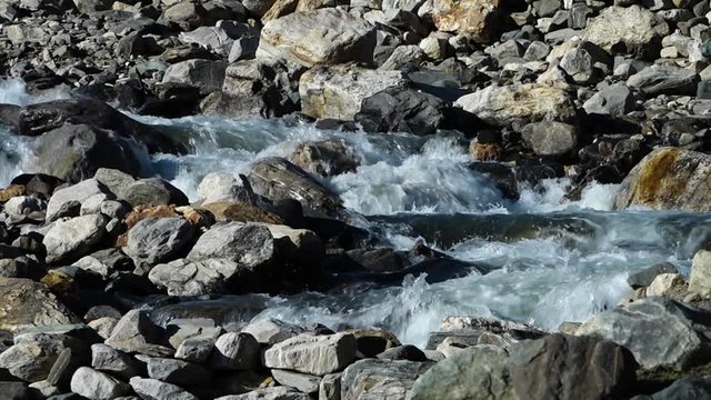 A steady, extreme close up shot of a small waterfall flowing away between the stones. 