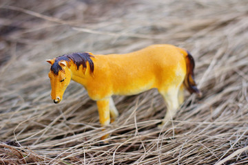 toy horse in nature photographed as real among the dry grass like haystacks