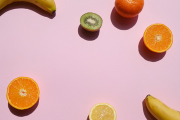 Colorful tropical fruits and slices on a pink background, sunlight, top view
