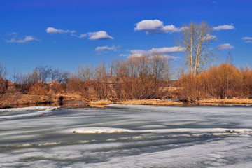 Early Spring landscape melts ice on a small river at the edge of the village.