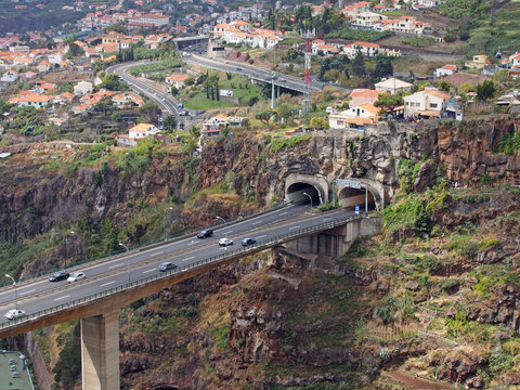 an aerial landscape view of the motorway bridge in funchal entering a tunnel in the valley with buildings and streets of the city