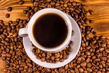 Cup of hot coffee and scattered coffee beans on wooden table. Top view