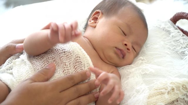 4K Selective focus close up shot of asian mother hands holding and cuddles her female newborn baby that sleeping to comfort and relaxed. Mother take care her newborn child with love.
