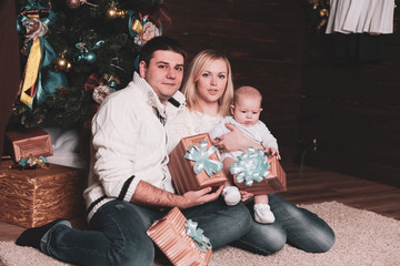 Obraz na płótnie Canvas happy family with gift boxes sitting near Christmas tree on Christmas eve