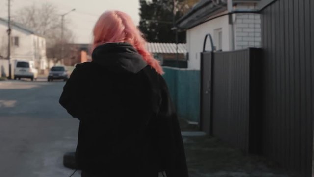 Portrait of young hipster girl with pink hair walking down the street at sunny day