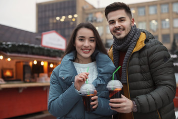 Young couple with cups of mulled wine at winter fair. Space for text