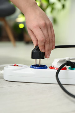 Woman inserting power plug into extension cord on floor indoors, closeup. Electrician's professional equipment