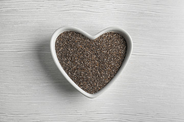 Heart shaped bowl with chia seeds on wooden background, top view