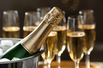 Fototapeta Bottle of champagne in bucket with ice and glasses on blurred background, closeup. Space for text obraz