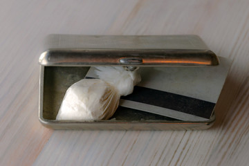 dose of cocaine in a plastic bag and a card inside an open cigarette case, against a light background, a blur, a haze