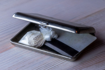 dose of cocaine in a plastic bag and a card inside an open cigarette case, on a light background, toning