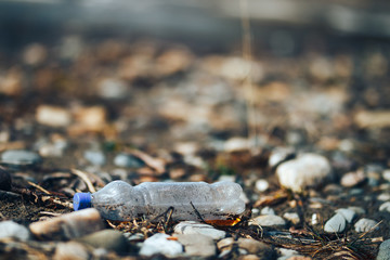 Environmental pollution plastic bottle with blue lid brown liquid inside on the beach among stones and sand
