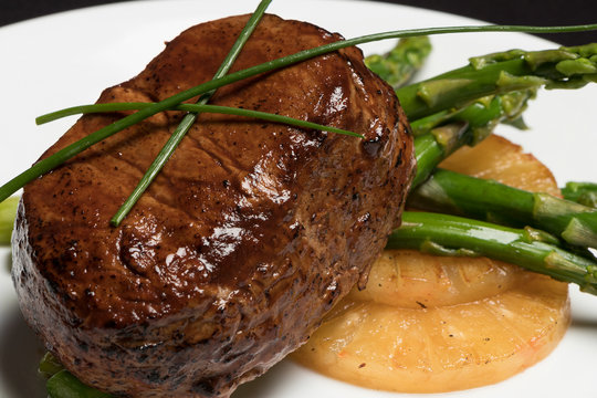 carne con esparragos y pi&ntilde;a en plato blanco y fondo negro