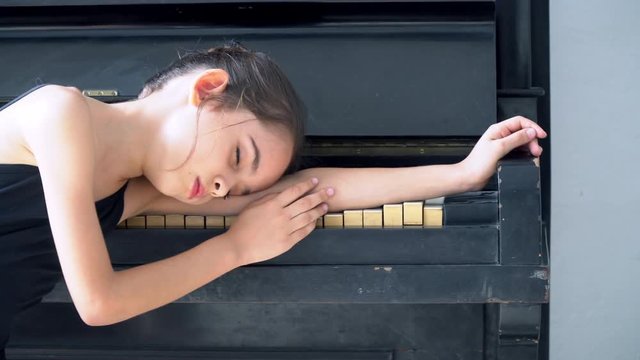 4K Video Selective focus medium close up dolly shot of young little ballerina girl in black leotard sleeping alone in the room on black piano.