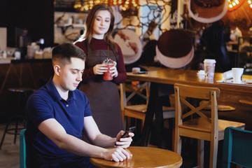 Portrait of cheerful young friends looking at smart phone while sitting in cafe. Mixed race people sitting at a table in restaurant using mobile phone.