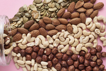 Different types of nuts and seeds in a glass jar on pink background, top view