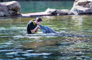 Cute teenage girl kissing a bottlenose dolphin on the nose in a beautiful ocean lagoon. Young girl loving Marine life in a natural setting