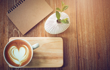 Fototapeta na wymiar Top view, latte art coffee on wooden table with book and small tree in ceramic vase background, vintage color tone