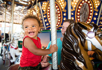 Cute mixed race little boy enjoying a ride on a fun carnival carousel. A happy boy Smiling and having fun riding a carousel ride at the summer carnival - obrazy, fototapety, plakaty