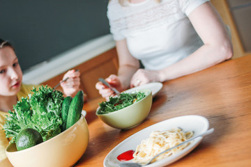 Tween girl and her mother eating vegetable salad and pasta at home