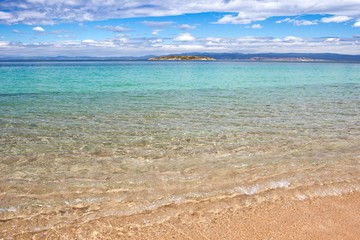 Crystal clear water, rippling gently on the shore gradually turns a pale turquoise and then blue as it reaches the island on the horizon.