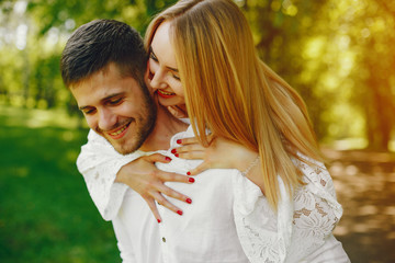 A beautiful and gentle girl with light hair and a white dress is walking in a sunny summer forest with her handsome guy in a white shirt and dark pants