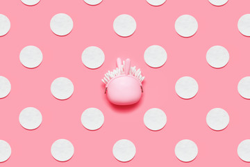 A little cosmetic bag-Easter bunny with cotton buds inside on a candy pink background in the center of pattern of eggs symbolizing Easter eggs. Minimal Easter pink concept.  Hygiene products.