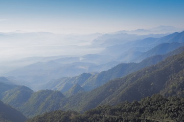 Mountain view morning on top of Doi Ang Khang above many hills and green forest cover with soft mist and blue sky background, Doi Angkhang, Chiang Mai, northern of Thailand.