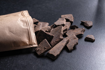 Natural chocolate without sugar from grated cocoa beans, in eco packaging on a dark background
