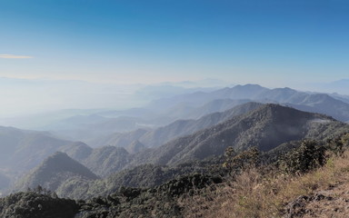 Obraz premium Mountain view morning on top of Doi Ang Khang above many hills and green forest cover with soft mist and blue sky background, Doi Angkhang, Chiang Mai, northern of Thailand.
