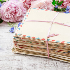 Stack of vintage love letters and pink peonies in the background.