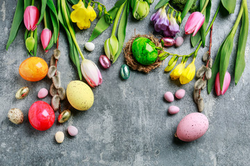 Colorful flowers and painted Easter eggs on grey, stone background