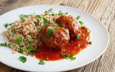 meet cutlets in tomato sauce garnished with  buckwheat porridge decorated with parsley on wooden table