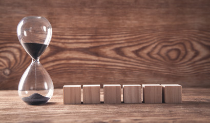 Hourglass with wooden cubes on wooden background.