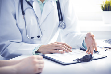Fototapeta premium Doctor and female patient sitting at the desk and talking in clinic near window. Medicine and health care concept. Green is main color