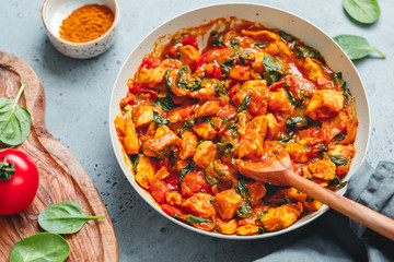 Bombay chicken curry with spinach, tomato and onion in a white frying pan on a kitchen table. Indian traditional cuisine.