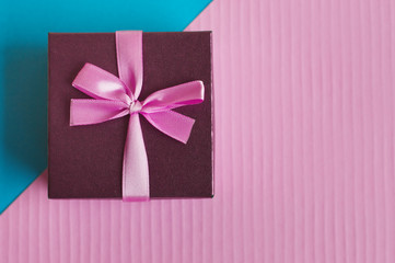 Small gift box with pink ribbon and bow on a colorful blue and pink background, copy space