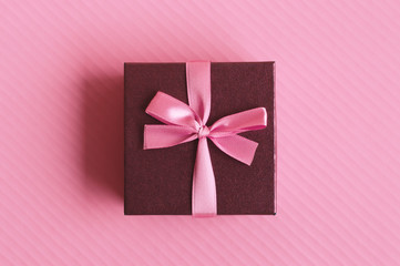 One small decorative gift box with pink ribbon on pink background, top view