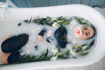 An elegant girl lies in a bathroom with flowers. Beautiful woman in black dress. Pregnant lady in a milk bath