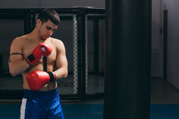 Muscular hardworking fighter in red boxing gloves practicing with punching bag, training strength and endurance. The Concept of a Sport, Boxing and Martial Arts.