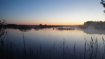 Fototapeta na wymiar Morning dawn of the sun through the mist over the water. Early morning in the forest on the river.