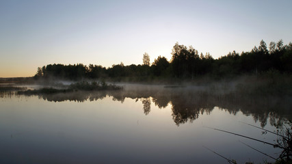 Obraz na płótnie Canvas Morning dawn of the sun through the mist over the water. Early morning in the forest on the river.