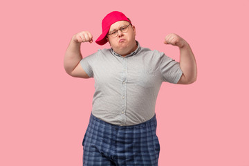 Funny comic overweight man dressed in casual wear shows his muscles with confident expression, aims...