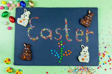 Easter concept multicolored candies are laid out in the form of Easter on a dark blue background with chocolate bunny and eggs