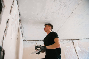 A man removes old paint from the ceiling with a spatula