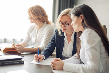 Three caucasian female students or interns in white shirts , intern using laptop, working on pc, studying in university, typing, browsing websites, apps, writing report, chatting in social network