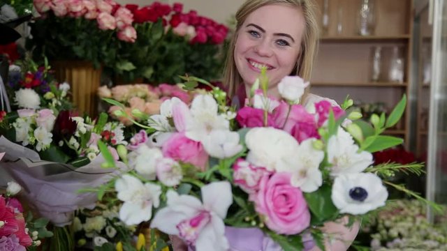 Smiling young florist woman gives a beautiful bouquet of roses to the camera, focus on a face. Flower business concept.
