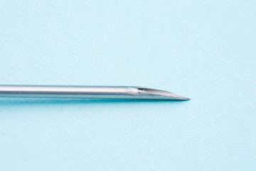 peak of an hypodermic needle isolated on blue surface, macro view