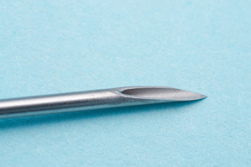 peak of an hypodermic needle isolated on blue surface, macro view